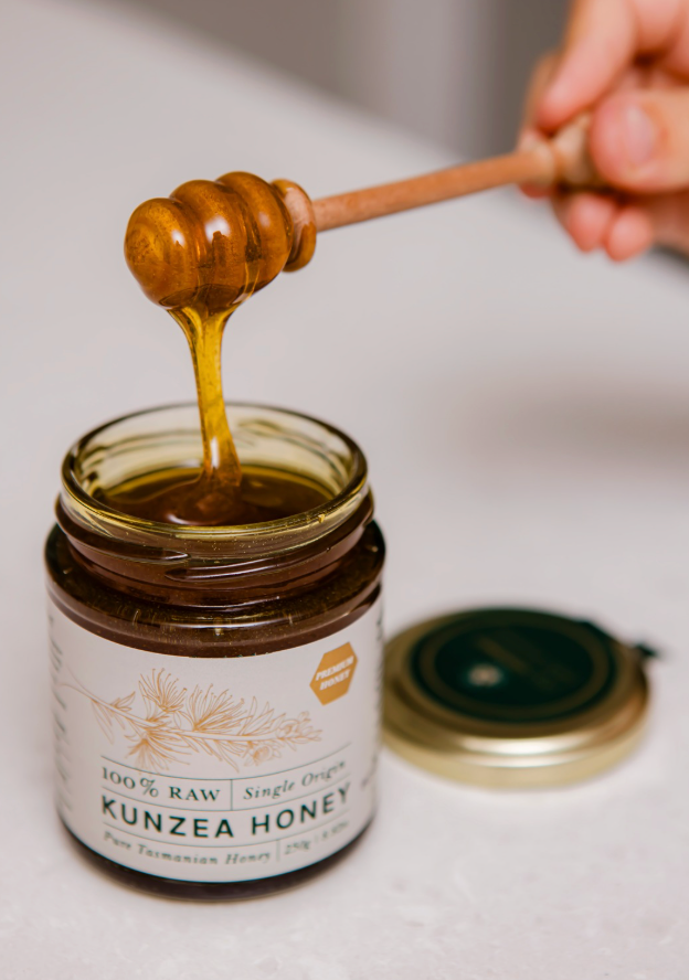 Honey dipper drizzling Kunzea Honey into an open jar
