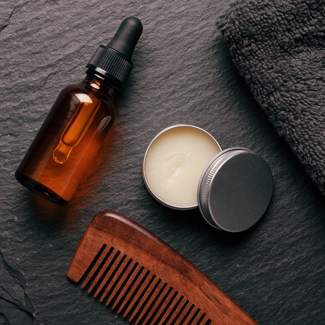 An amber dropper bottle beside an open tin of solid balm and a wooden comb